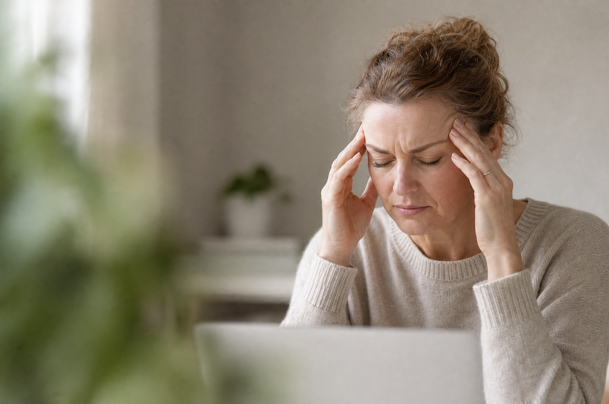 A woman at her desk in the afternoon, eyes closed, fingertips at her temples